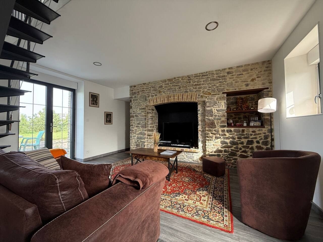 A living room with a stone fireplace, a sofa, a coffee table, and a large window.