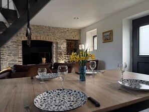 A dining area with a wooden table set for four, a stone fireplace, and a staircase. - La Bergerie Lodge, 200 meters from the sea (Pirou)
