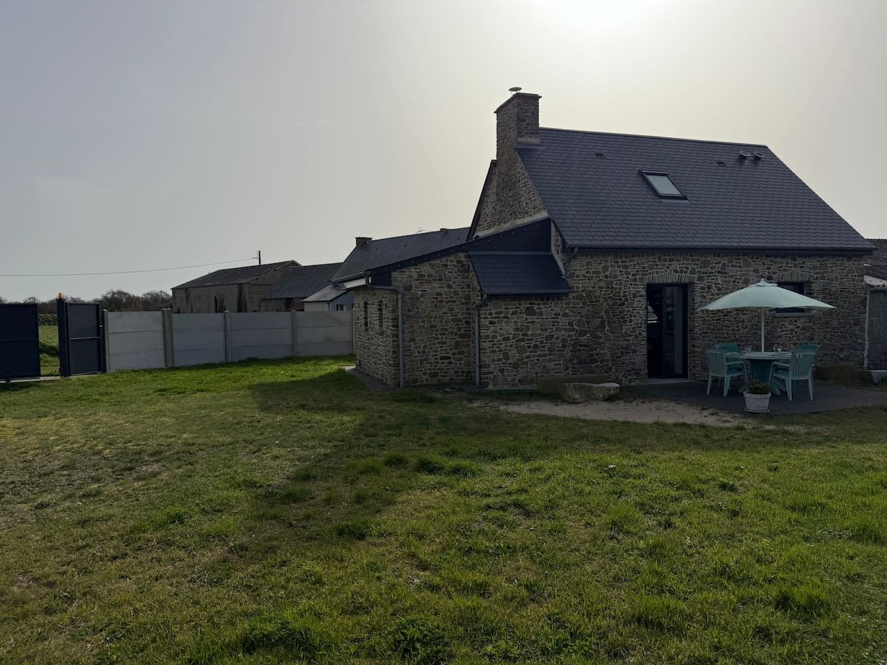 Ein Steinhaus mit geneigtem Dach, einer Terrasse mit Sitzgelegenheiten und einem Rasen.