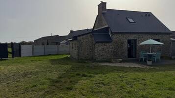 Ein Steinhaus mit geneigtem Dach, einer Terrasse mit Sitzgelegenheiten und einem Rasen.