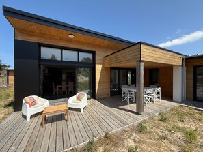 Ein modernes Haus mit einer Holzterrasse, Sitzgelegenheiten im Freien und einem großen Schiebeglastür.