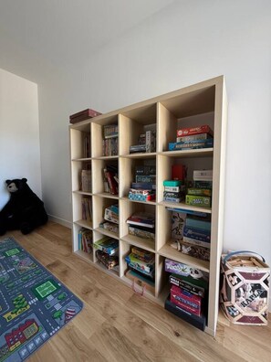 Quarto com estante repleta de jogos de tabuleiro e livros.