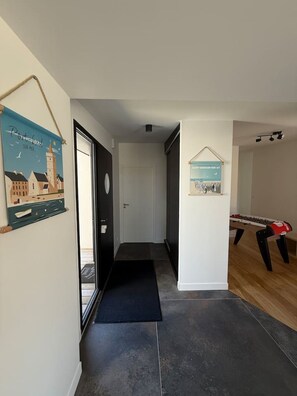 A hallway with a dark mat leading to a door, a poster on the wall, and a foosball table in the background. - California-style villa, oceanfront (Saint-Germain-sur-Ay)