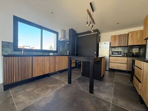 A modern kitchen with a large window, dark cabinetry, and a central island. - California-style villa, oceanfront (Saint-Germain-sur-Ay)