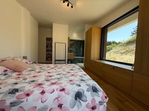 Ein Schlafzimmer mit einem großen Bett, einem Holzschrank und einem Fenster mit Blick auf eine natürliche Landschaft.