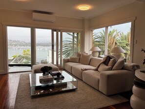 Ein geräumiges Wohnzimmer mit einer großen Couch, einem Glastisch und Blick auf eine Marina durch raumhohe Fenster.
