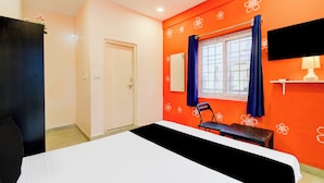 A hotel room with a bed, a desk, a chair, a window with curtains, a wall-mounted TV, and a door. - Hotel O Chandanagar Formerly Nakshatra (Hyderabad)