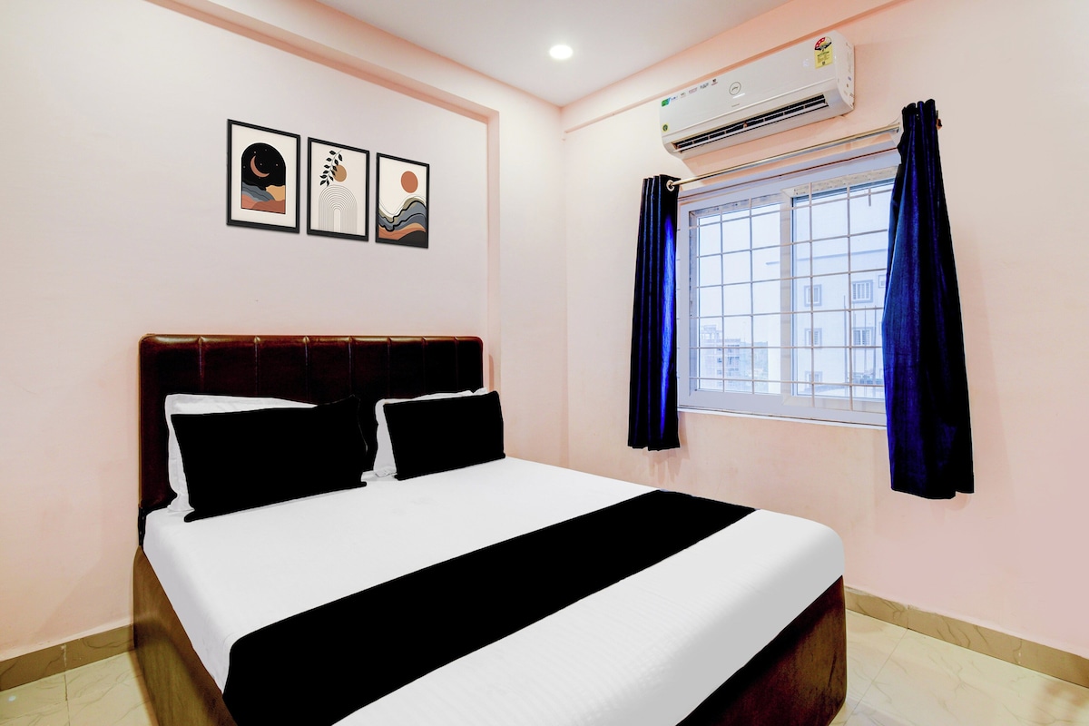 Een hotelkamer met een bed, een airconditioning, een raam met gordijnen, en drie ingelijste foto's aan de muur.