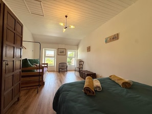 Ein Zimmer mit einem Bett, einem Holzschrank, einem Stuhl, einem Tisch und einem Deckenventilator.