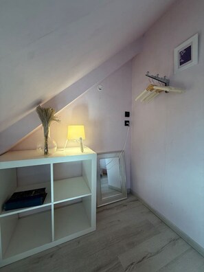 A room with a sloped ceiling, a white console table with a lamp, a mirror, and a hanging clothes rack. - Family home near the beach, 5 bedrooms, pool table, garden (Bretteville-sur-Ay)