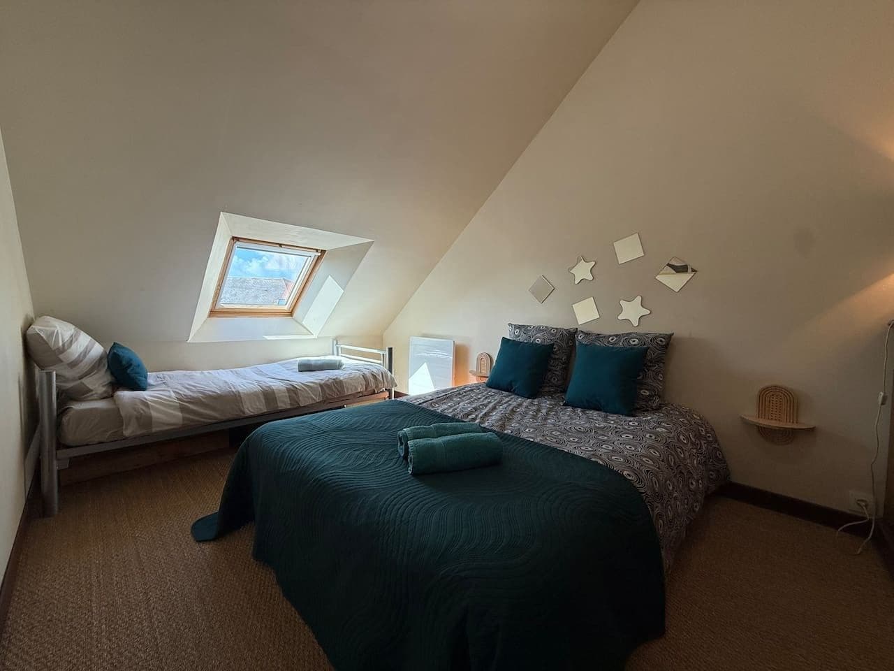Une chambre avec un lit superposé, un lit simple, un puits de lumière et des œuvres d’art décoratives sur les murs.