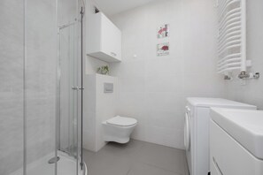 A modern bathroom with a glass shower enclosure, a toilet, and a washing machine.