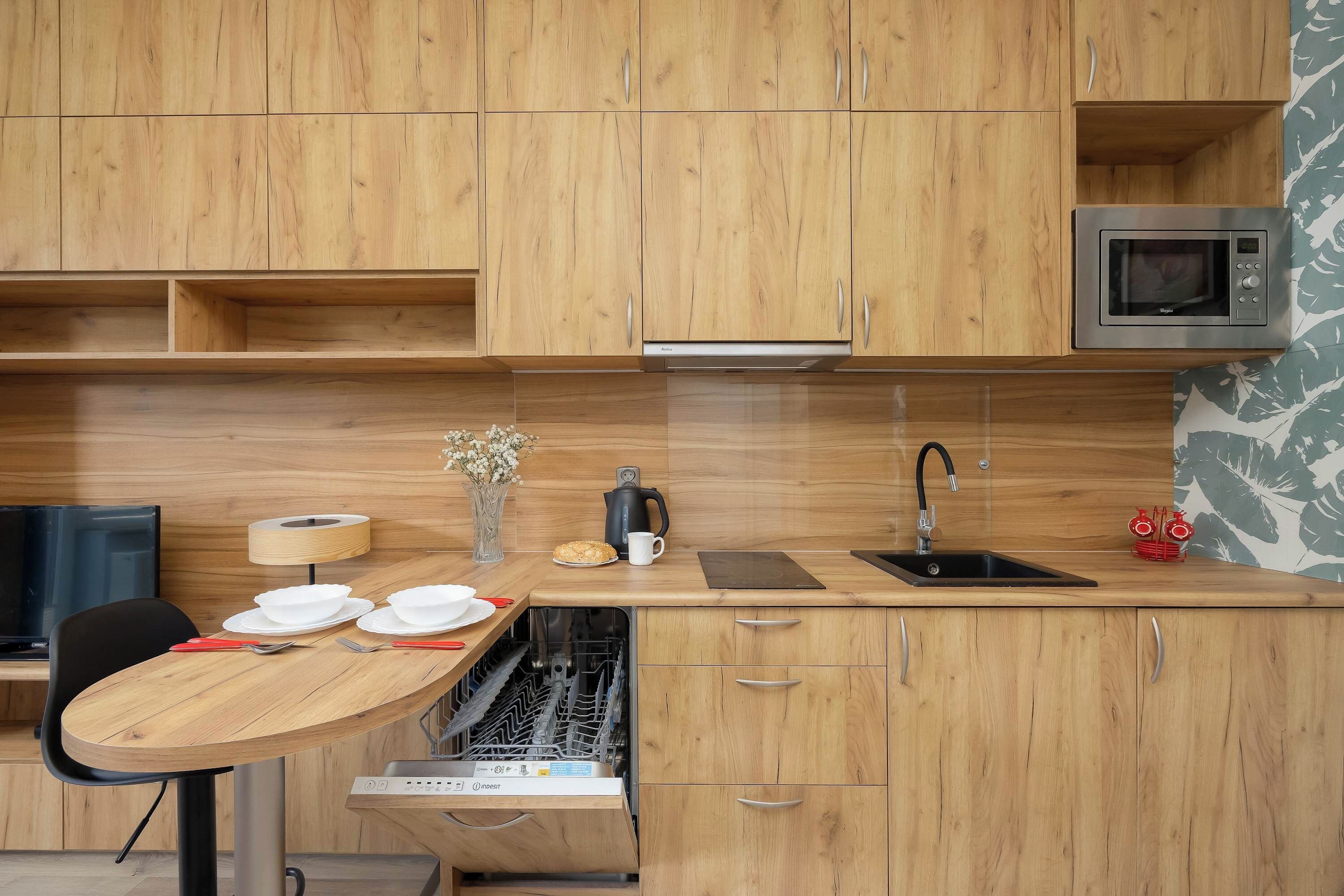 A compact kitchen with wooden cabinets, a microwave, a sink, and a dishwasher.