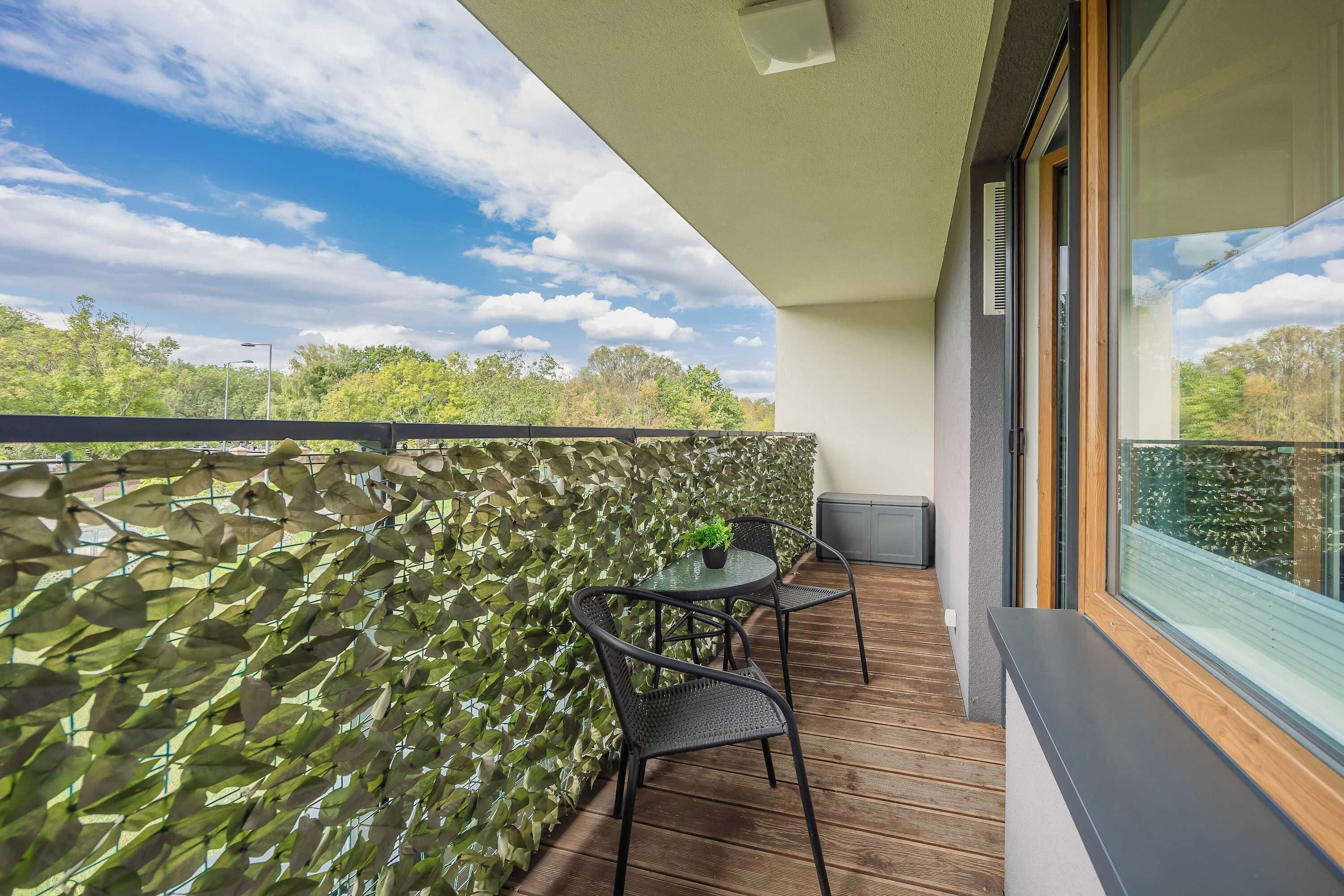 A balcony with a stone wall, a table with two chairs, and a view of trees and sky.