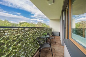 A balcony with a stone wall, a table with two chairs, and a view of trees and sky.