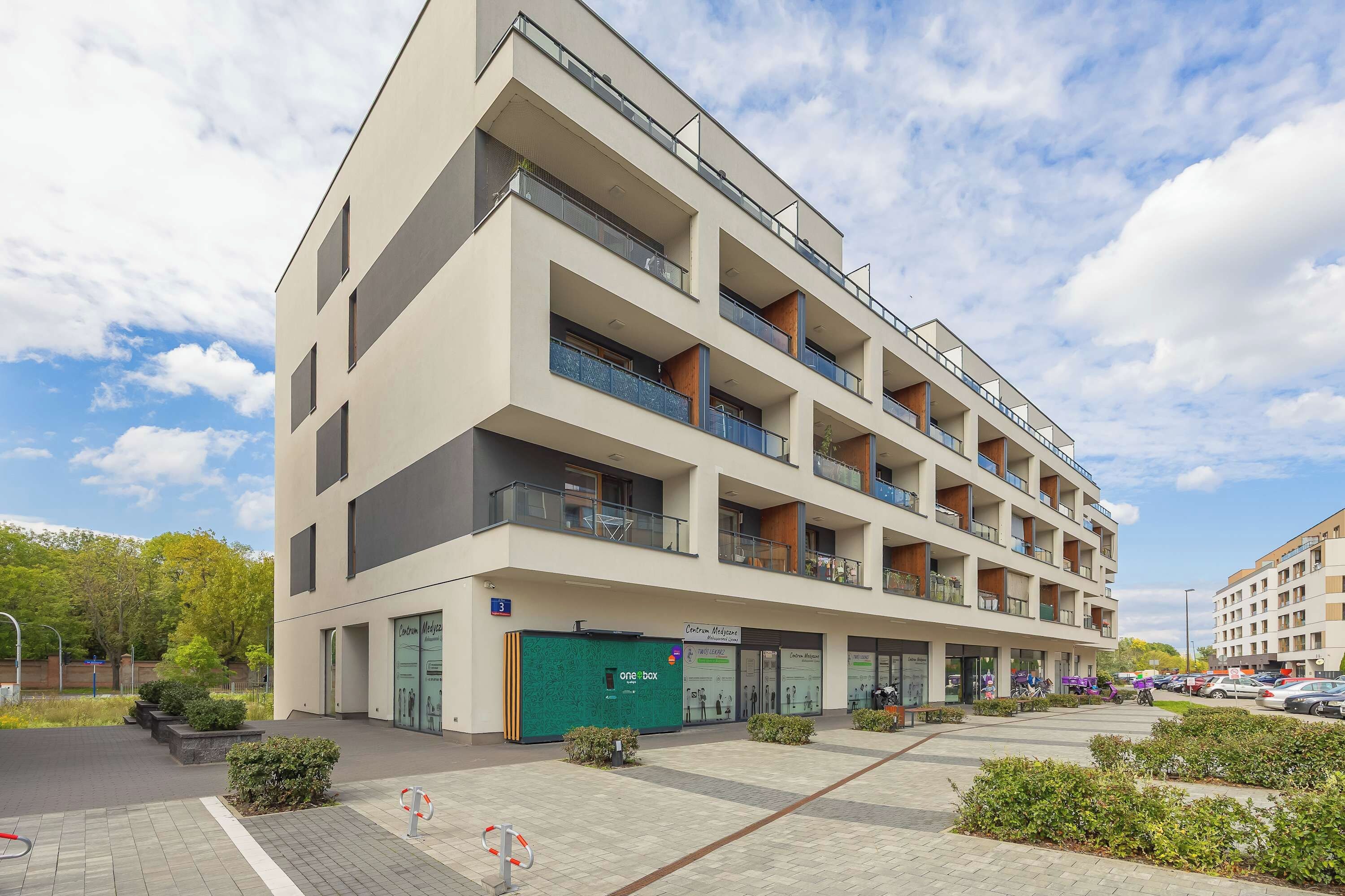 A multi-story building with balconies, a green storefront, and a parking area.