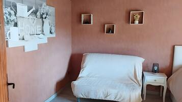 Un dormitorio con cama, una mesita de noche, un estante en la pared con objetos decorativos y una puerta con picaporte.