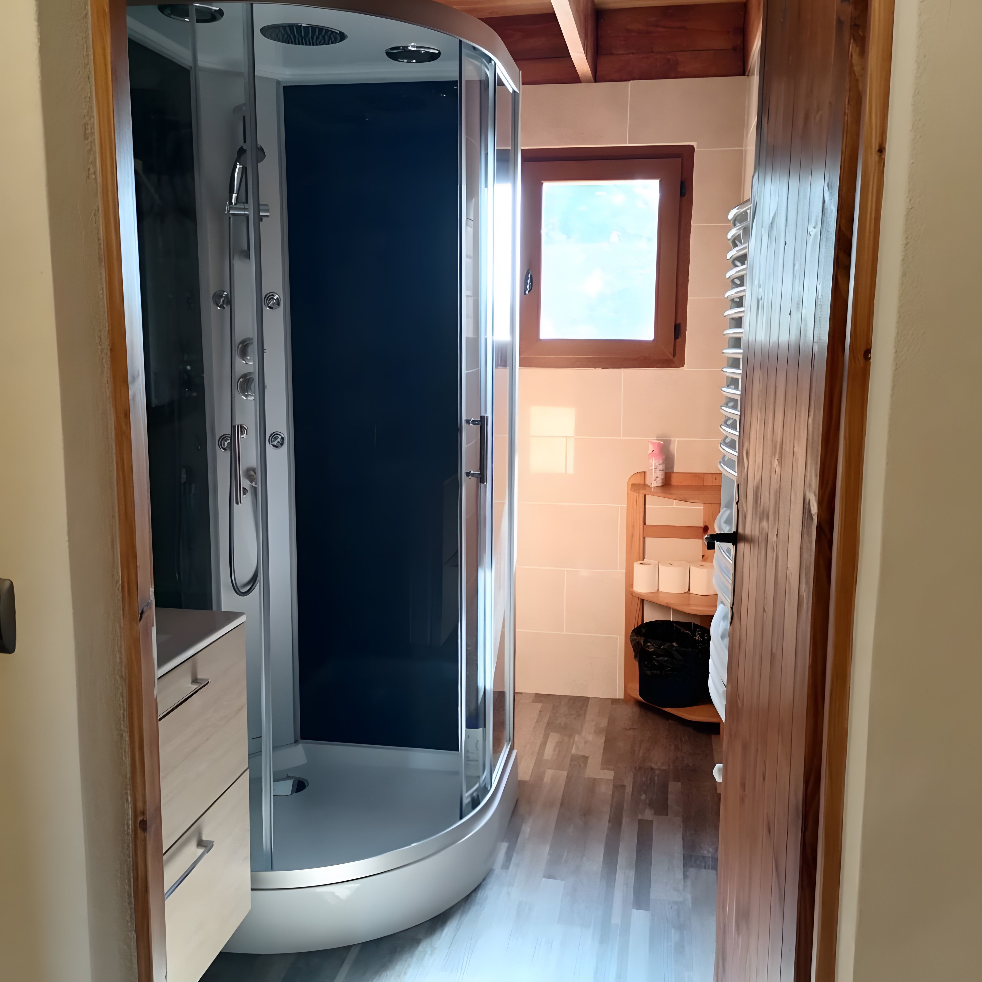 Un bagno con doccia vetrata, pavimento in legno e una piccola finestra.