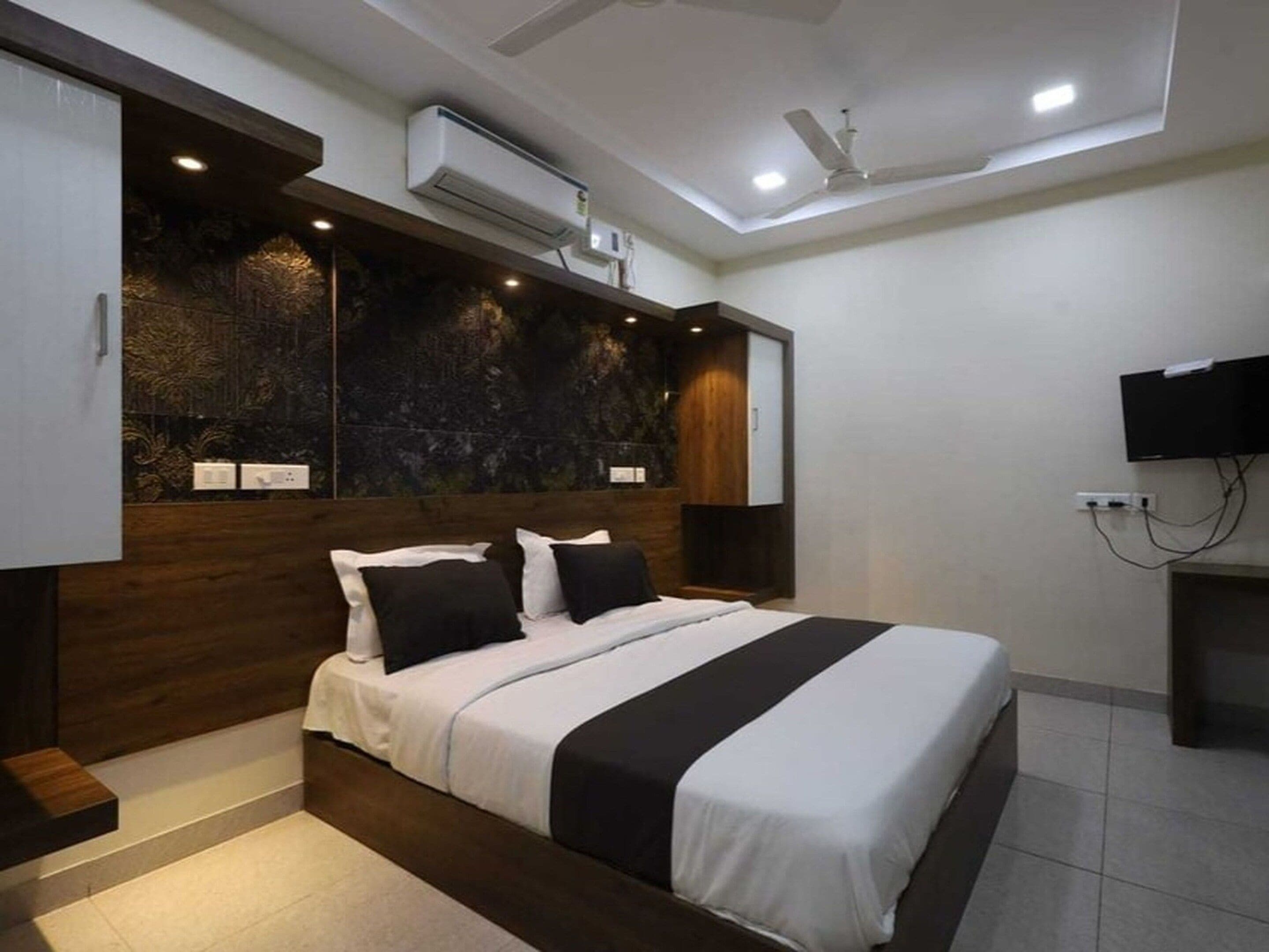 A modern bedroom with a bed, built-in wardrobe, air conditioning unit, ceiling fan, and a flat-screen TV.