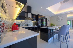 Uma cozinha moderna com armários pretos, um eletrodoméstico vermelho e uma ilha de vidro com banquetas.