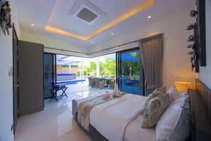 Ein modernes Schlafzimmer mit einem großen Bett, einer Glastür, die auf einen Balkon führt, und Blick auf einen Poolbereich.
