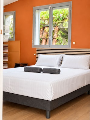Une chambre à coucher avec un lit, des oreillers et une fenêtre donnant sur des plantes.