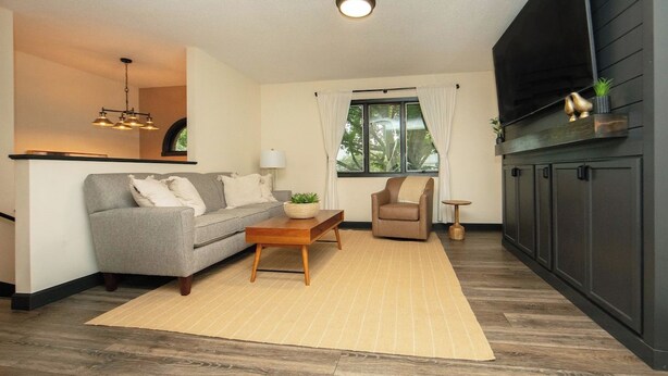 A living room with a sofa, coffee table, and armchair, a kitchen area with cabinets, and a window with curtains. - New Listing: Freshly updated and blocks from campus, downtown and trails (Waverly)