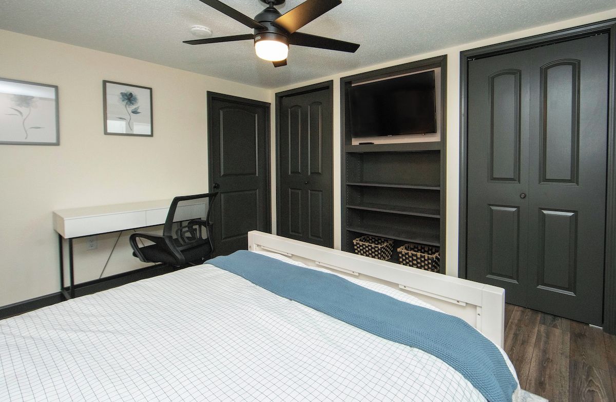 Quarto com cama, escrivaninha, cadeira, ventoinha no teto e estantes embutidas.