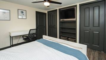 Quarto com cama, escrivaninha, cadeira, ventoinha no teto e estantes embutidas.