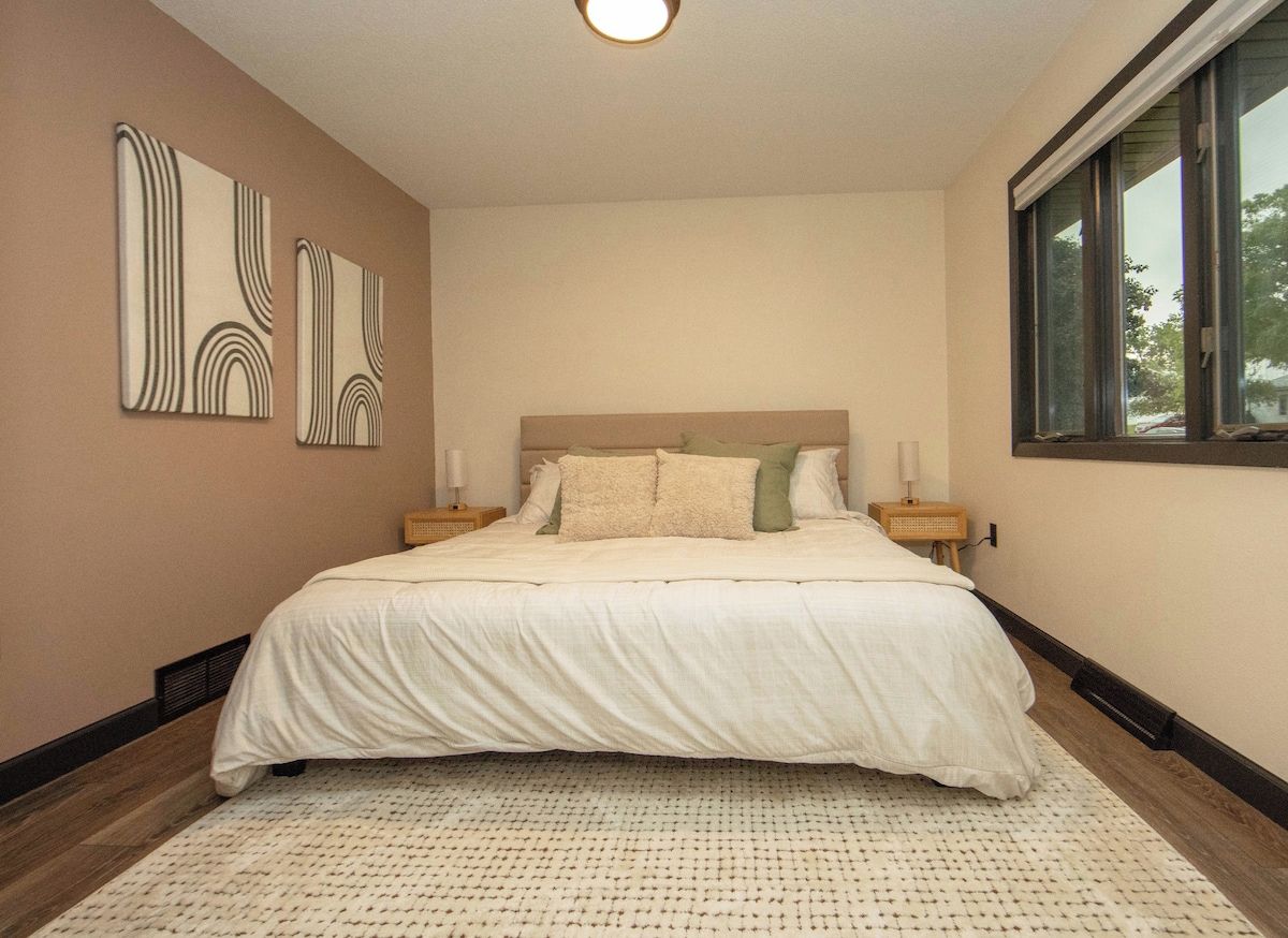 A bedroom with a large bed, a window, and wall art.