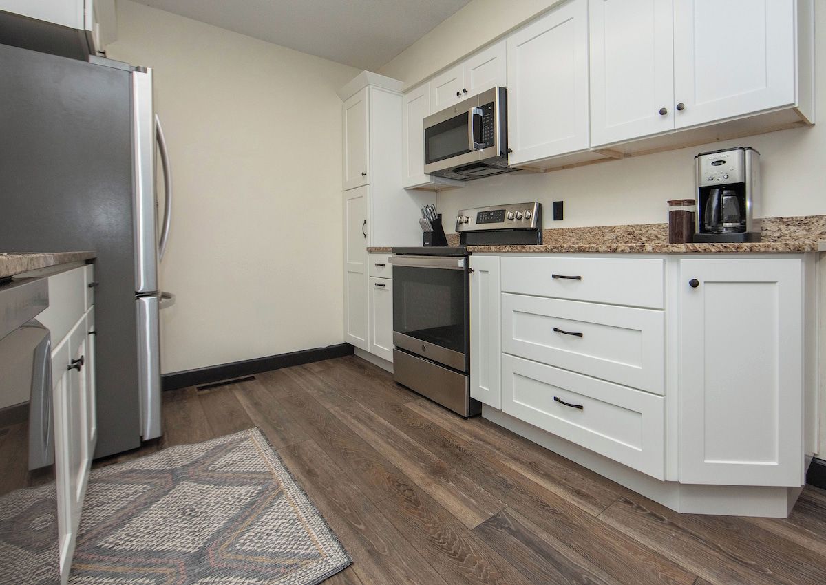 A kitchen with white cabinets, a stainless steel refrigerator, a microwave, an oven, and a coffee maker.