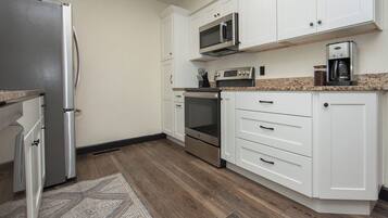 A kitchen with white cabinets, a stainless steel refrigerator, a microwave, an oven, and a coffee maker.