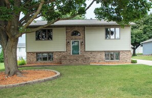 A two-story house with a brick facade, a green front door, and a small front yard with a tree and mulch. - New Listing: Freshly updated and blocks from campus, downtown and trails (Waverly)
