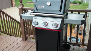 A Weber Spirit grill with a control panel and a side cabinet, placed on a wooden deck.