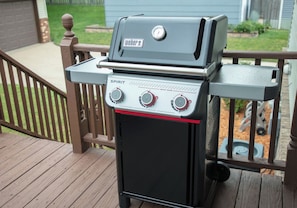 A Weber Spirit grill with a control panel and a side cabinet, placed on a wooden deck.