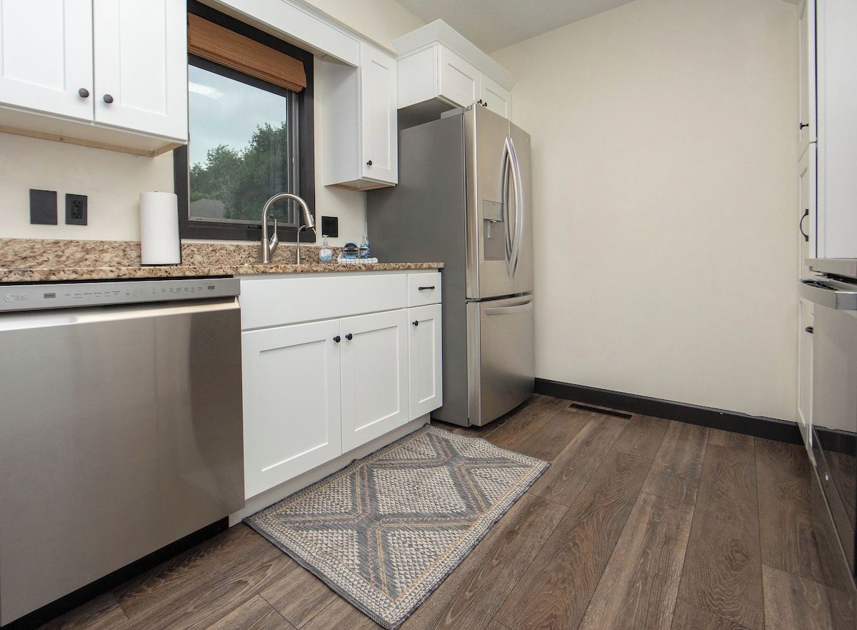 Una cocina moderna con armarios blancos, un refrigerador de acero inoxidable y un tapete estampado en el suelo.