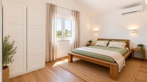 A bedroom with a wooden bed, a window with curtains, a wall-mounted air conditioner, and a bedside table with a plant.