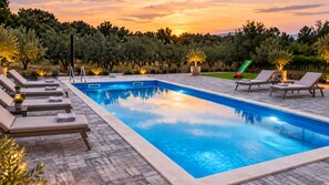 A rectangular pool with a tiled edge, surrounded by lounge chairs and potted plants.