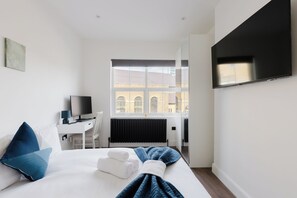 Een hotelkamer met een bed, een bureau met een computer, een televisie en een raam met uitzicht op gebouwen.