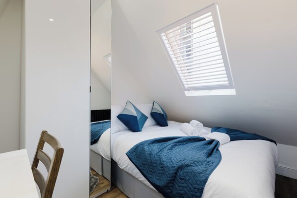 A bedroom with a bed, pillows, a blanket, a window, and a chair. - Modern 4BDR Flat in the Heart of Wandsworth (Greater London)