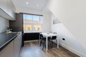 A compact kitchen with a window, a dining table with chairs, and a radiator. - Modern 4BDR Flat in the Heart of Wandsworth (Greater London)