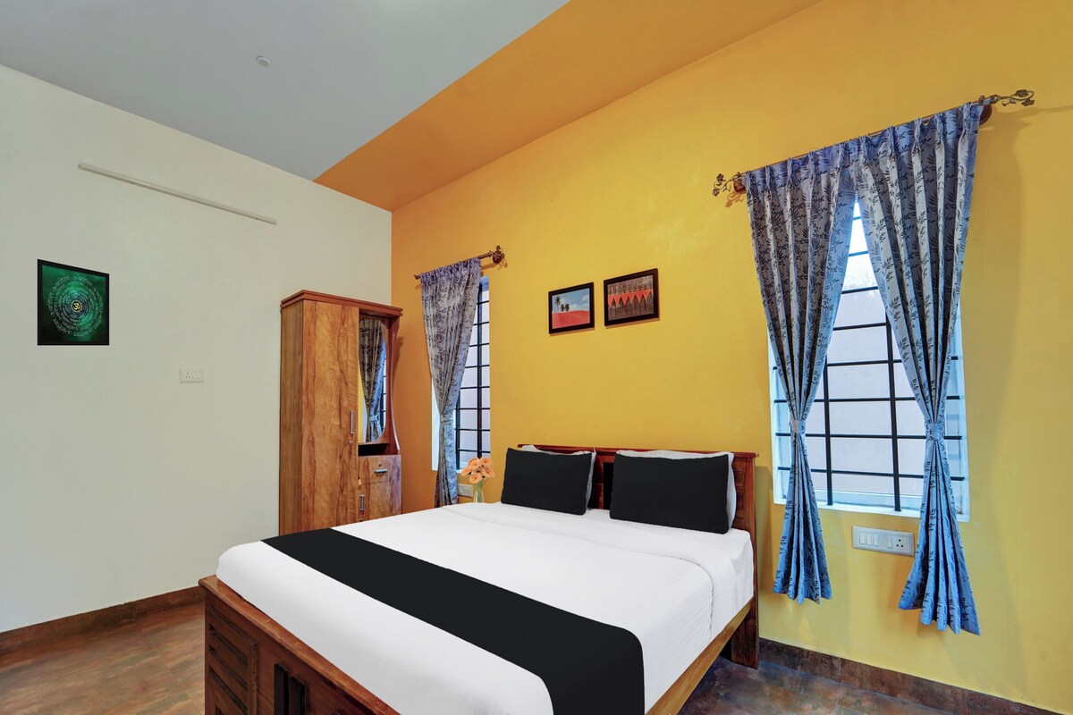 A bedroom with a bed, two framed pictures, a wooden wardrobe, and a window with curtains.