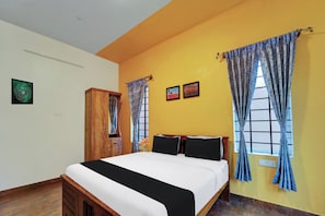 A bedroom with a bed, two framed pictures, a wooden wardrobe, and a window with curtains. - Super Hotel O Rose Garden Ooty (Ootacamund)