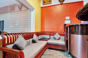 A seating area with a wooden bench and cushioned seats, a small table, and a decorative wall with a clock. - Super Hotel O Rose Garden Ooty (Ootacamund)