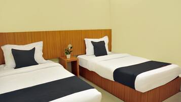 Two single beds with white and black bedding, a wooden headboard, a small bedside table with a plant, and a plain wall.