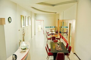 A conference room with a long table, red chairs, framed pictures on the walls, and a view through a glass door.