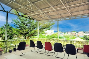 A covered outdoor seating area with chairs, a view of buildings, and greenery.
