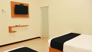 A hotel room with two beds, a wooden shelf, a small table, a mirror, and a door.