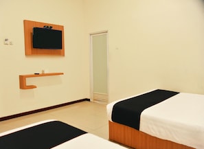 A hotel room with two beds, a wooden shelf, a small table, a mirror, and a door.