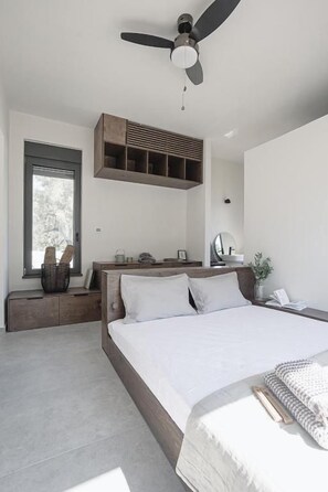 A modern bedroom with a bed, a ceiling fan, a window, and a built-in shelf. - NIMA Suites (Palairos)